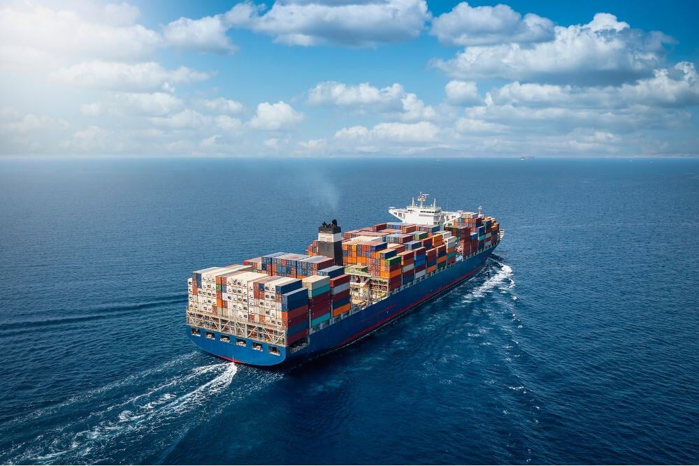 A large container cargo ship travels over calm, blue ocean.