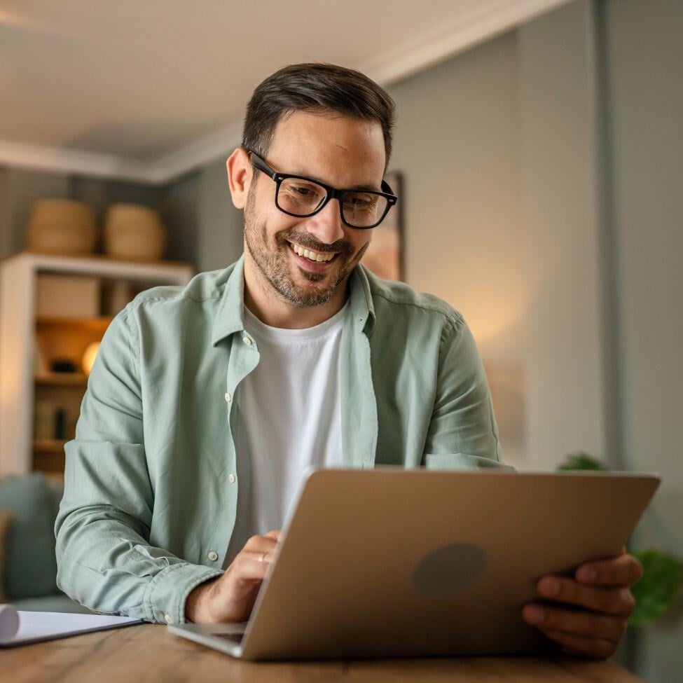 Man sat at home, smiling at his laptop.